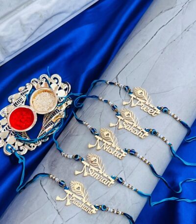 Custom Peacock Feather Name Rakhi with gold engraved name plate, evil eye beads, and premium blue silk thread for Raksha Bandhan.