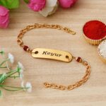 Custom gold name bracelet Rakhi with Rudraksha beads, engraved name plate, and premium adjustable chain.