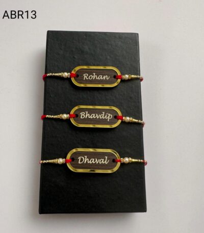 Personalized wooden name Rakhi with gold frame, pearl bead accents, and traditional red thread for Raksha Bandhan.