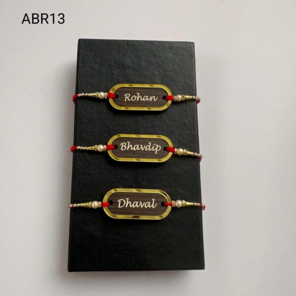 Personalized wooden name Rakhi with gold frame, pearl bead accents, and traditional red thread for Raksha Bandhan.