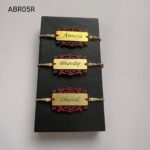 Personalized brushed gold name plate Rakhi with decorative designer base, pearl bead accents, and traditional red thread for Raksha Bandhan.