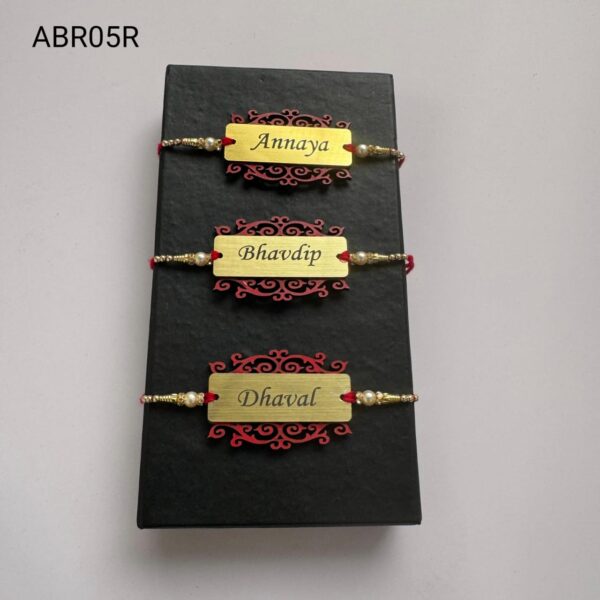 Personalized brushed gold name plate Rakhi with decorative designer base, pearl bead accents, and traditional red thread for Raksha Bandhan.