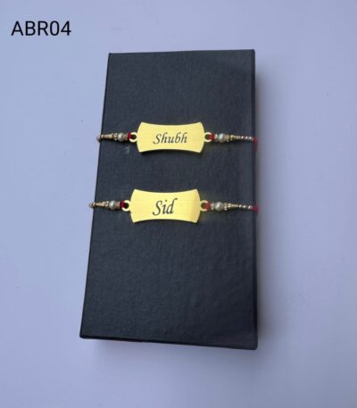 Personalized classic gold name plate Rakhi with custom engraving, pearl bead accents, and traditional red thread for Raksha Bandhan.