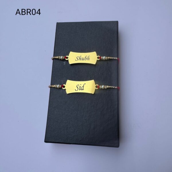 Personalized classic gold name plate Rakhi with custom engraving, pearl bead accents, and traditional red thread for Raksha Bandhan.