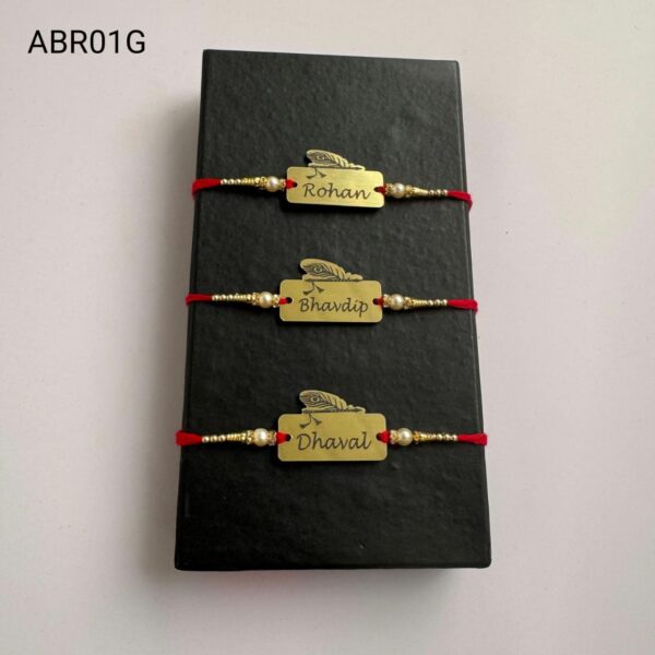 Personalized feather name plate Rakhi available in gold and silver finish with custom engraving, pearl beads, and traditional red thread.